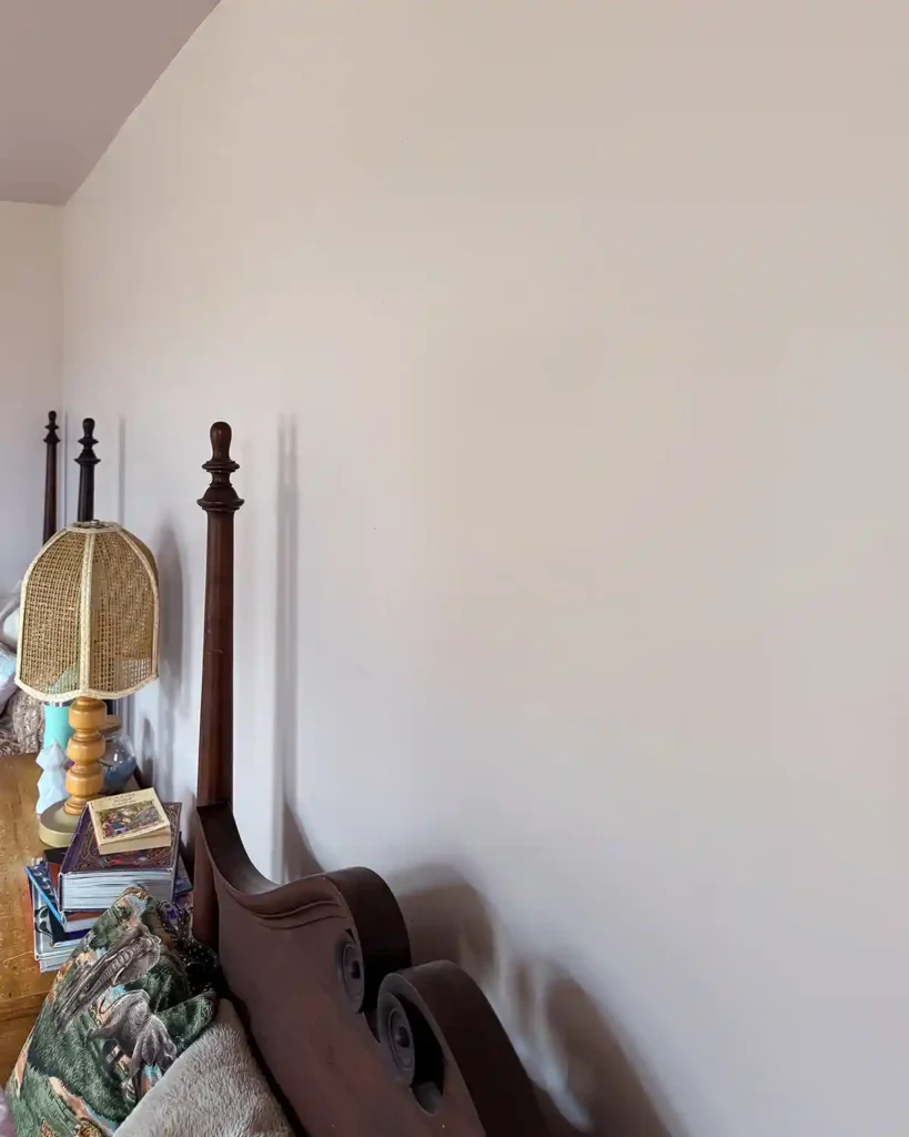 The repaired area of a bedroom wall after patching holes in the drywall, priming and painting the walls pink; bedroom headboard and dresser in the bottom of the picture