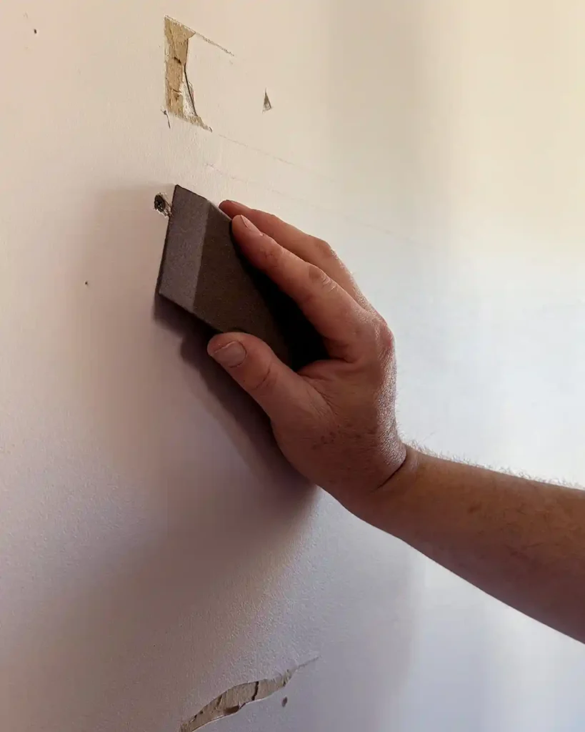 Sanding drywall with a sanding block before applying joint compound to get a smooth finish before patching the holes  in the damaged wall