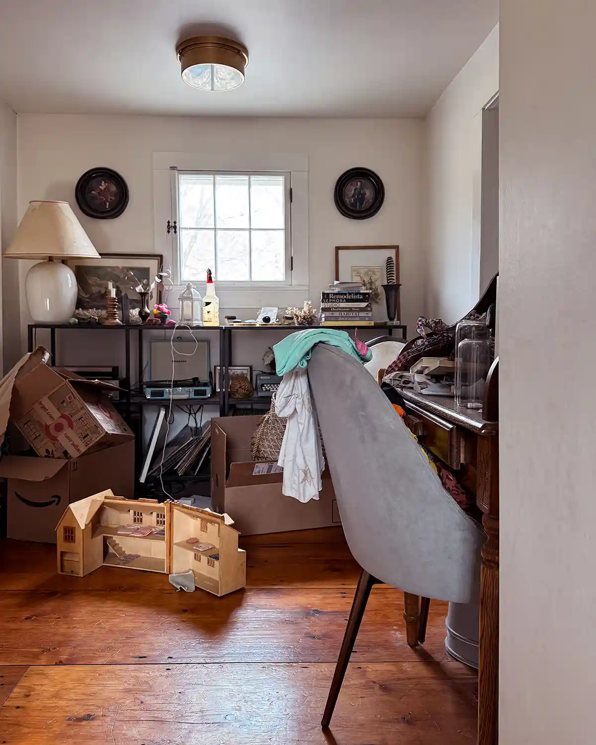 The end of hallway with too much stuff piled in it including boxes, clothes, toys, books, and more cluttering up the space on the floor, shelves, and desk
