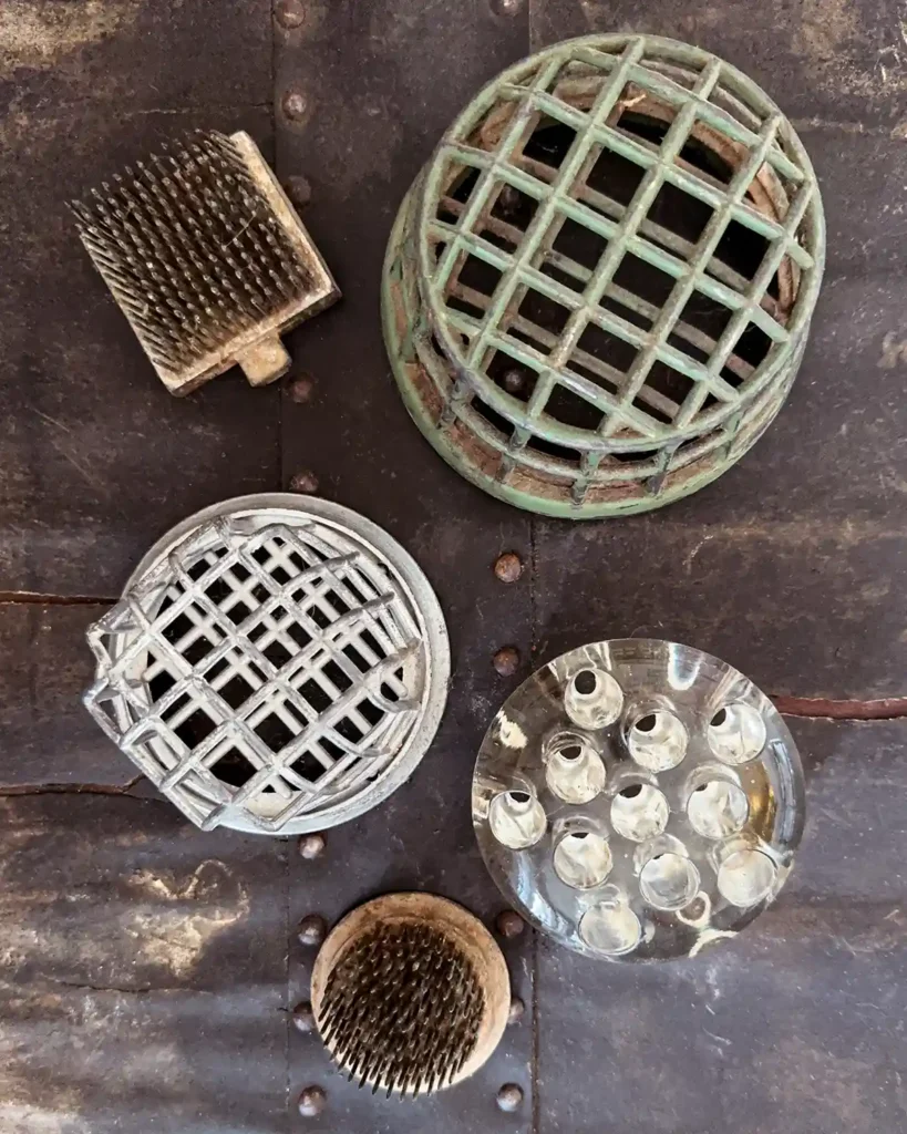 A collection of vintage flower frogs including metal pin frogs, metal cage frogs, and glass flower frogs