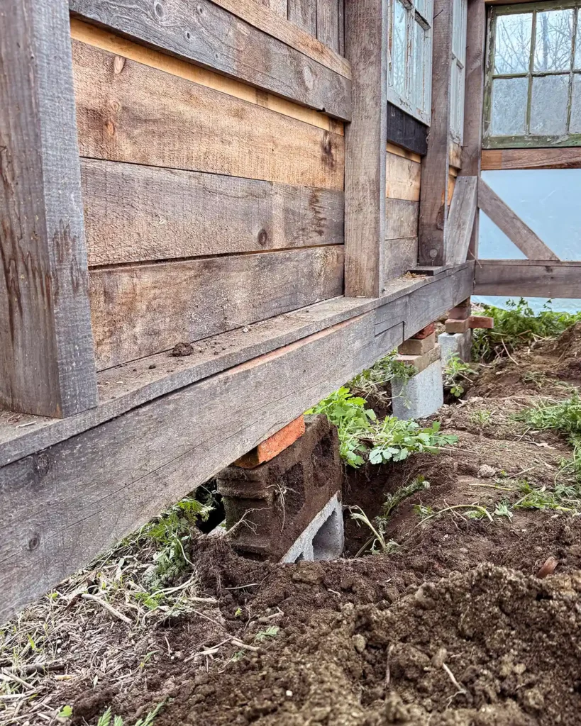 Adding concrete blocks underneath a greenhouse to help support it and keep the structure level after jacking it back up