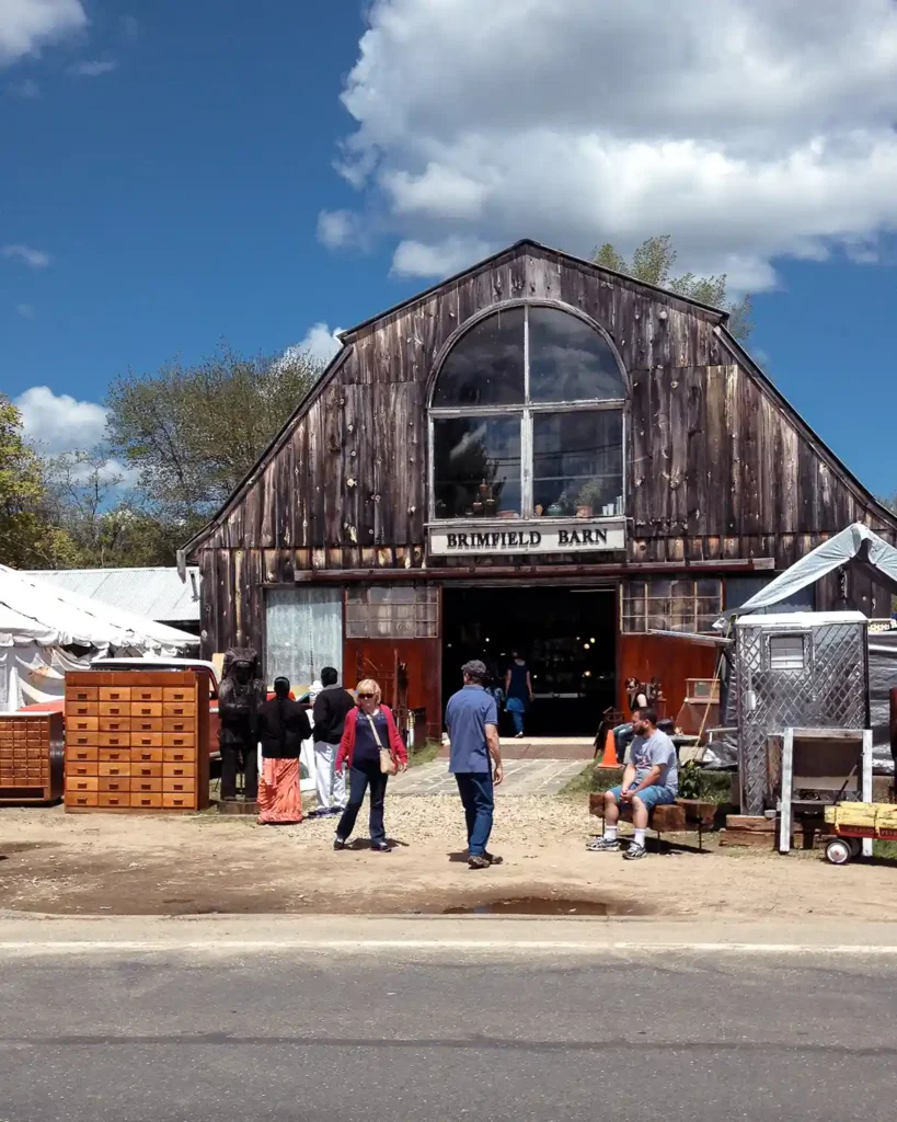 The iconic Brimfield Barn photographed from across the road; vintage furniture outside in front of the barn with shoppers all about