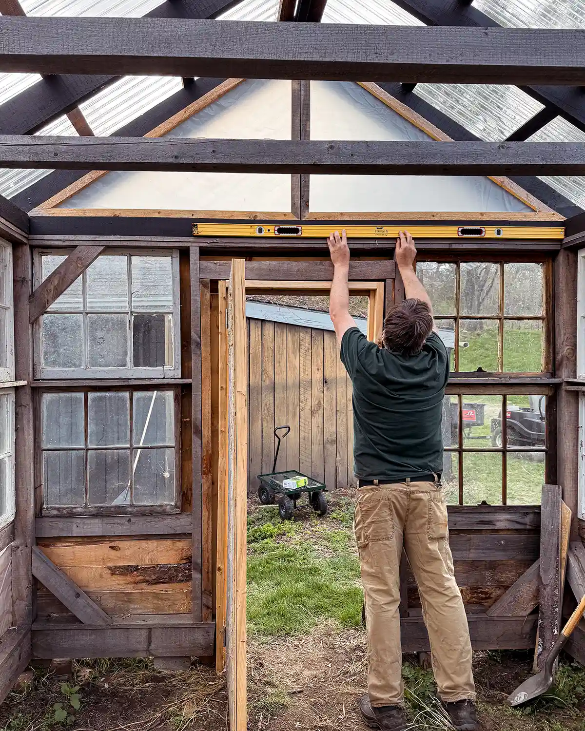 Using a long box beam level to check the levelness across the short end of a DIY window greenhouse over the door
