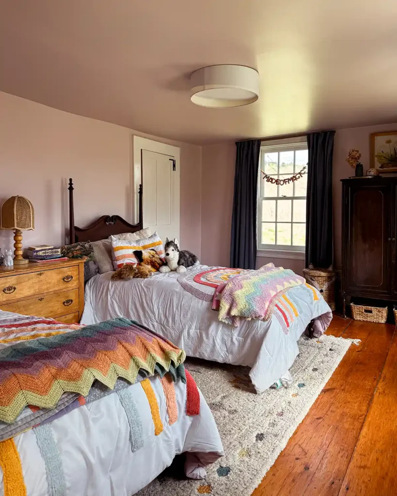 A girls shared bedroom with two vintage twin beds with rainbow comforters, painted pink