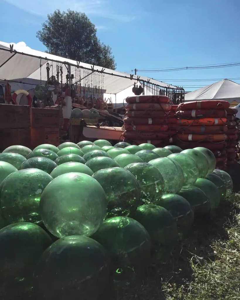 A pile of green glass floats and stacks of life preservers and a vintage seller's booth and tent at the Brimfield flea market