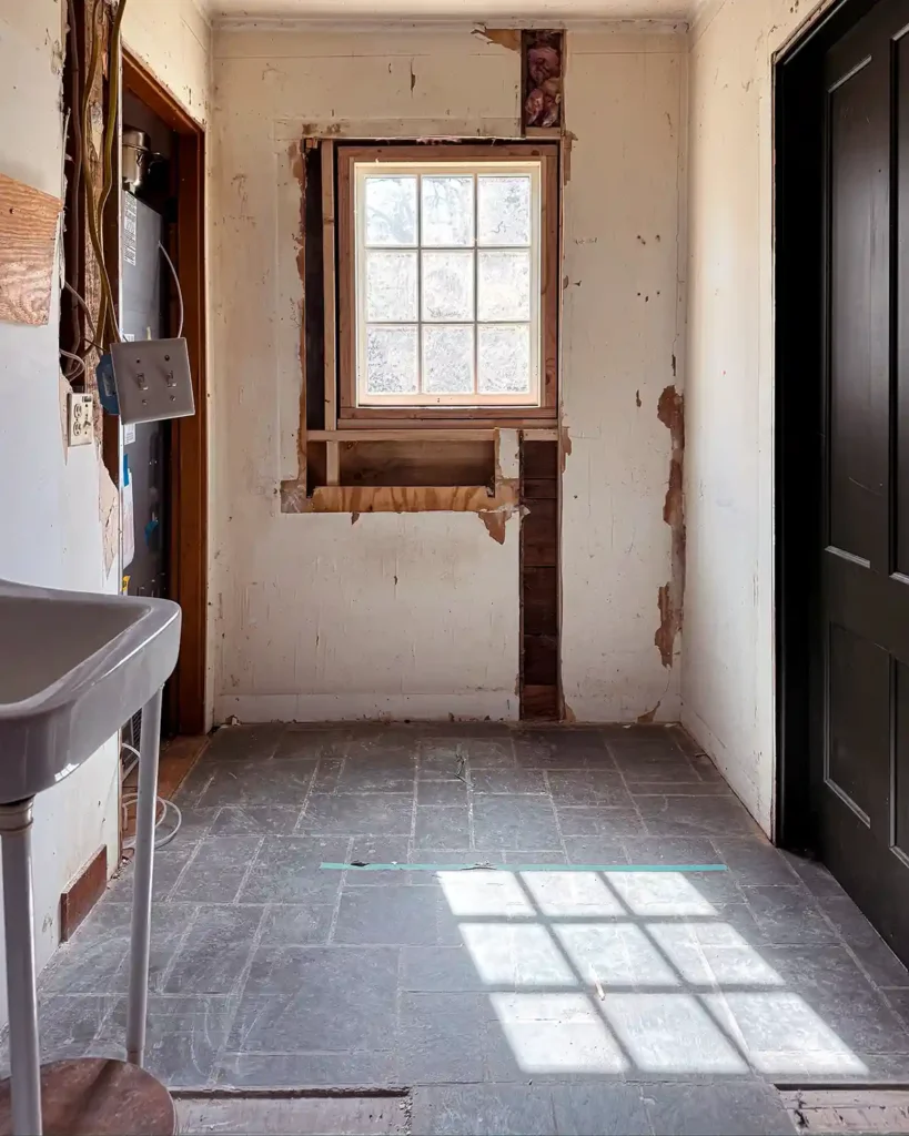 Demolition and renovation progress of a laundry room and bathroom combo with a wall removed and a new window at the end installed