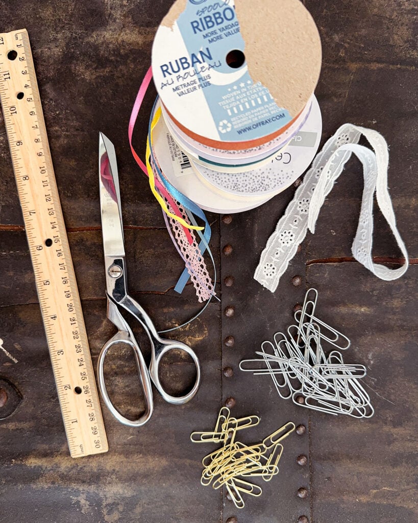 Paperclip bookmark making supplies including ribbon in various sizes and materials, paperclips (regular and jumbo size), fabric scissors, and a wooden ruler