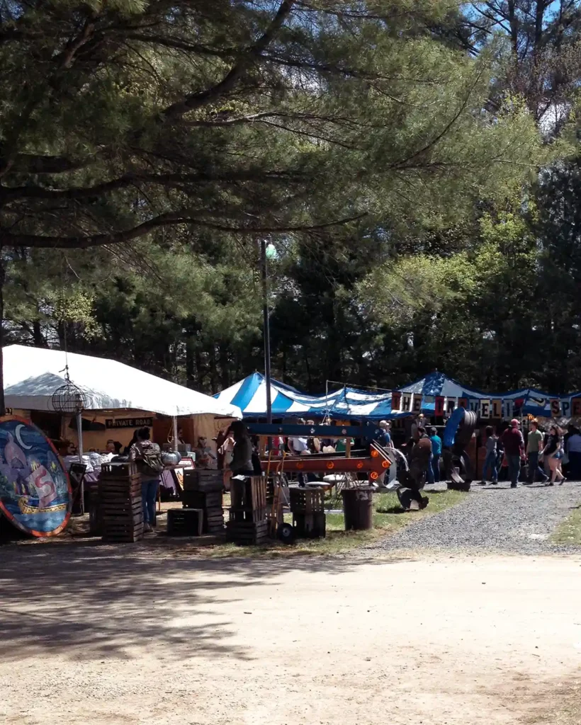 Vintage seller booths and tents set up along a wooded roadway at the Brimfield flea market and antique show