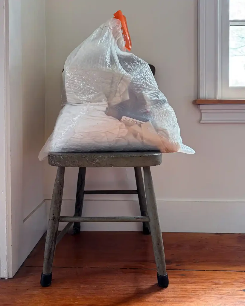 A full trashbag, sitting on a chippy green painted chair, after doing a decluttering sweep for trash throughout the house