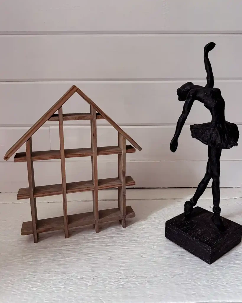 A vintage, unfinished, wooden house shelf to display small figurines and a black ballerina statue.