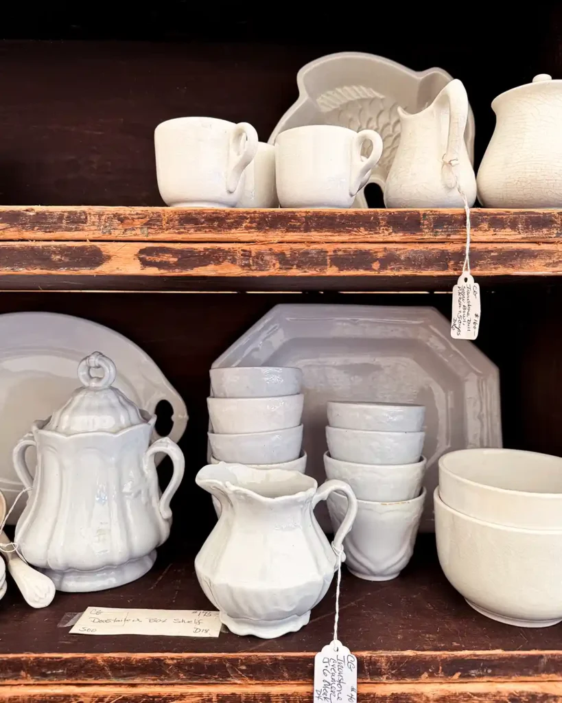 A collection of vintage ironstone on display shelves for sale at the Brimfield flea market