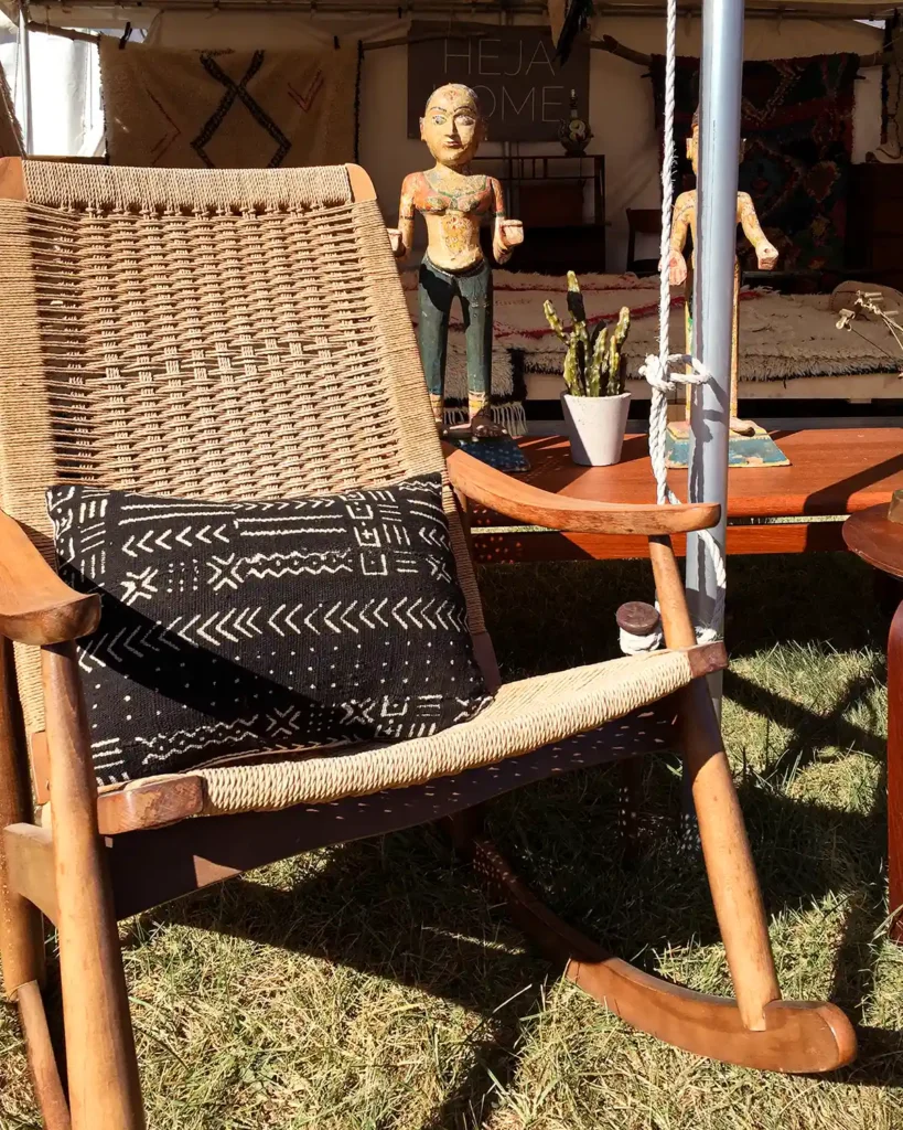 A vintage rocking chair with a black mudcloth covered pillow sitting on it in front of a vintage seller's tent at Brimfield