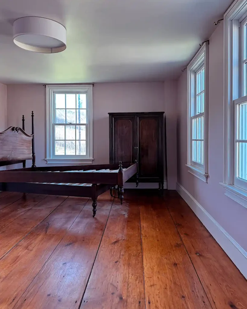 A bedroom with as much furniture, art, and other items removed as possible before painting a ceiling. All that remains is a large, antique wardrobe and a pair of twin antique bed frames stacked on top of each other