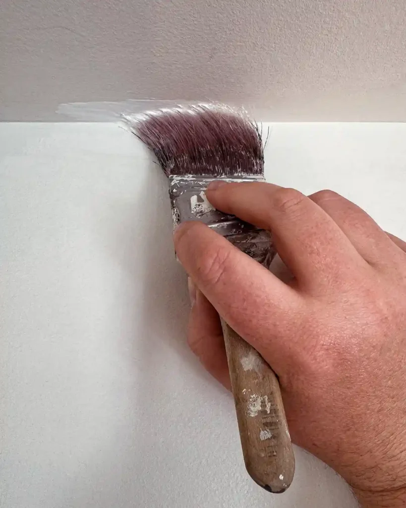 Using an angled brush to cut in white ceiling paint around the edge of the ceiling where it meets the wall
