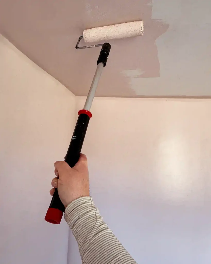 Painting a ceiling pink using a manual paint roller with an extension pole