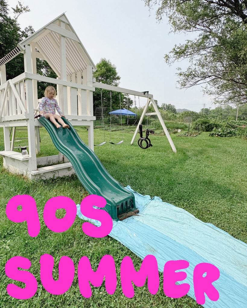Photo of a slip 'n slide at the bottom of a playground slide with a kid going down it with the text "90s summer" in hot pink letters across the bottom of the photo