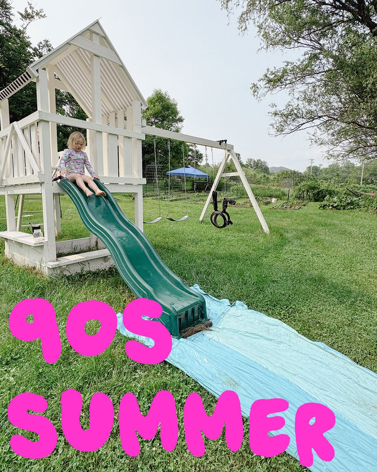 Photo of a slip 'n slide at the bottom of a playground slide with a kid going down it with the text "90s summer" in hot pink letters across the bottom of the photo