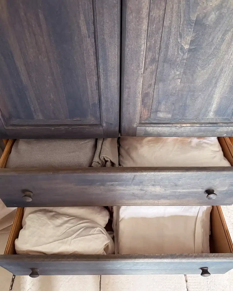A decluttered and organized blue linen cabinet drawers with just enough folded flat and fitted sheets for the beds in our home