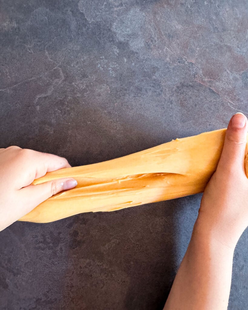A pair of hands stretching and pulling apart homemade orange slime