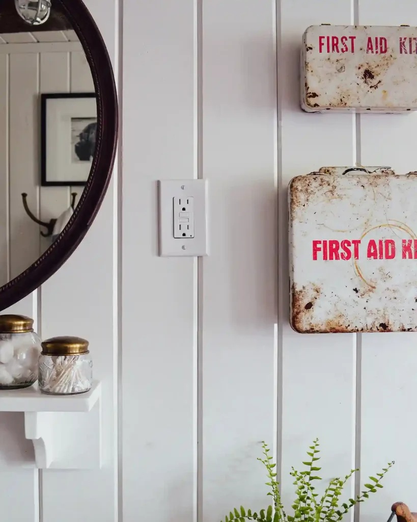 A pair of vintage first aid kits hanging in a bathroom against white, planked walls with a mirror and shelf peeking out from above the vanity