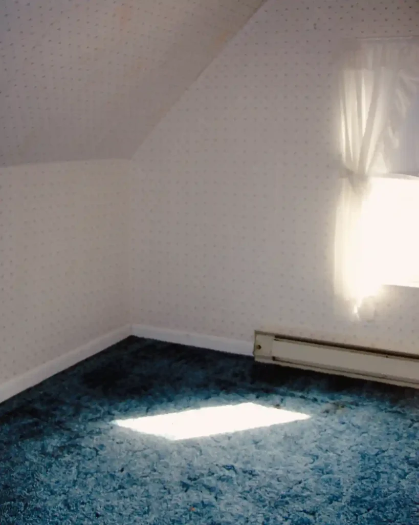 A dated bedroom with a blue shag rug and white patterned wallpaper with water damage before renovating and turning into a craft room