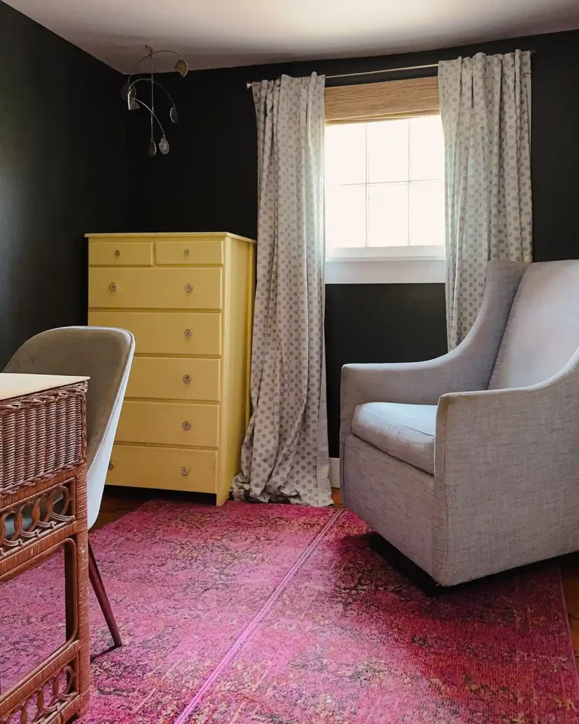 The initial home office furniture placement for a one-day room makeover featuring a pink rug, wicker desk with a fabric covered desk chair, tall yellow dresser in the corner, and former light blue nursery glider in the other corner