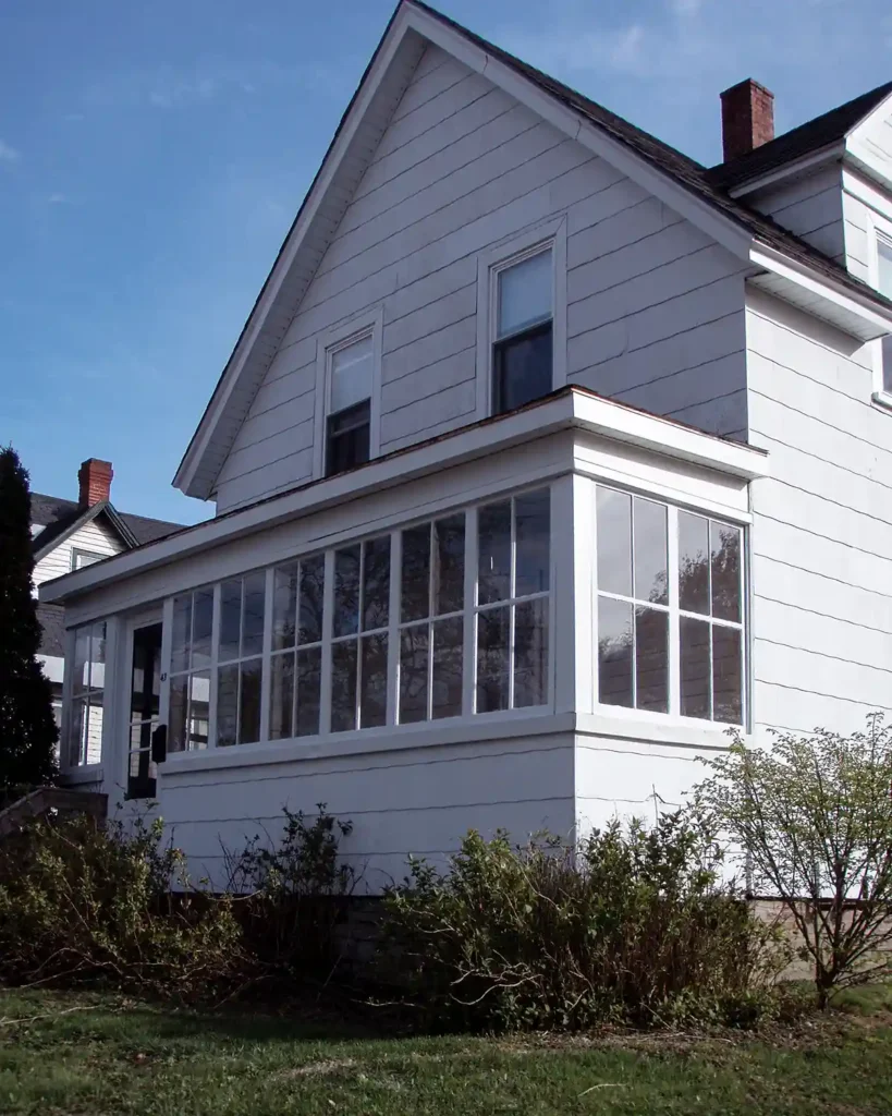 A white sided Maine farmhouse with a gable front end, dormers, and an enclosed front porch; before picture on the day we closed on the house