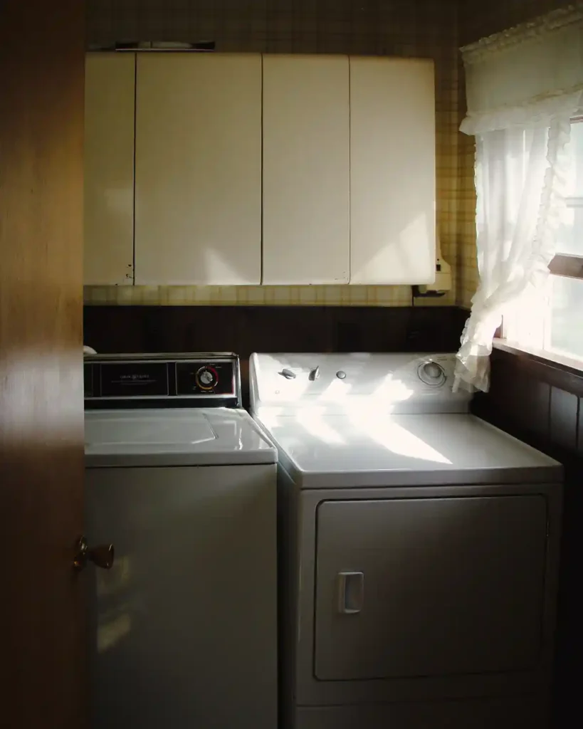 A vintage laundry room with old laundry appliances, metal cabinets, dark paneling, and yellow plaid wallpaper