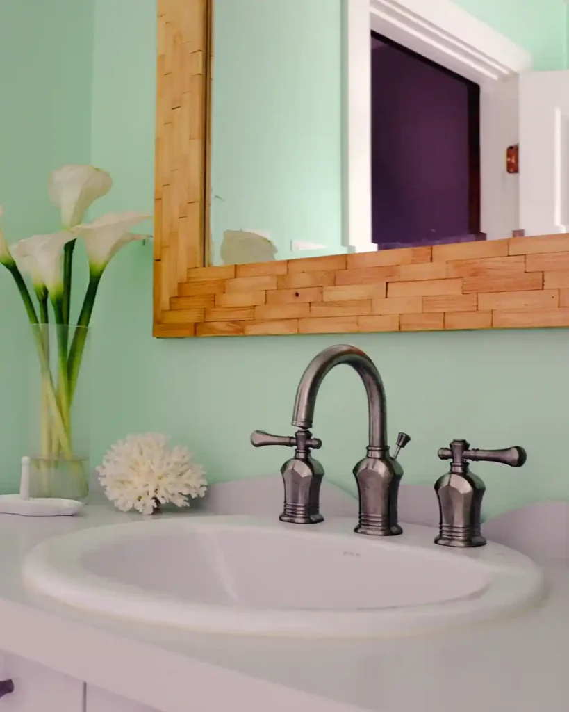 A wood tiled framed mirror hanging in a bathroom above a vanity with drop in sink