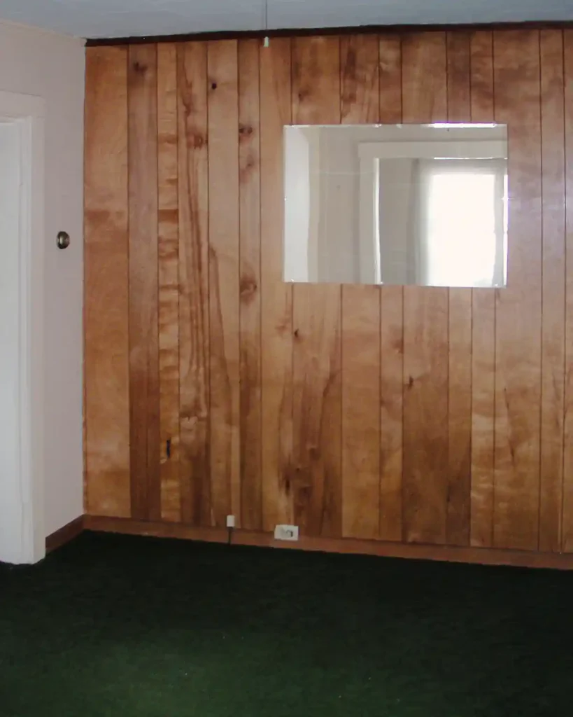 Parlor space before renovating featuring wood paneling, unframed mirror, and green rug before starting to renovate