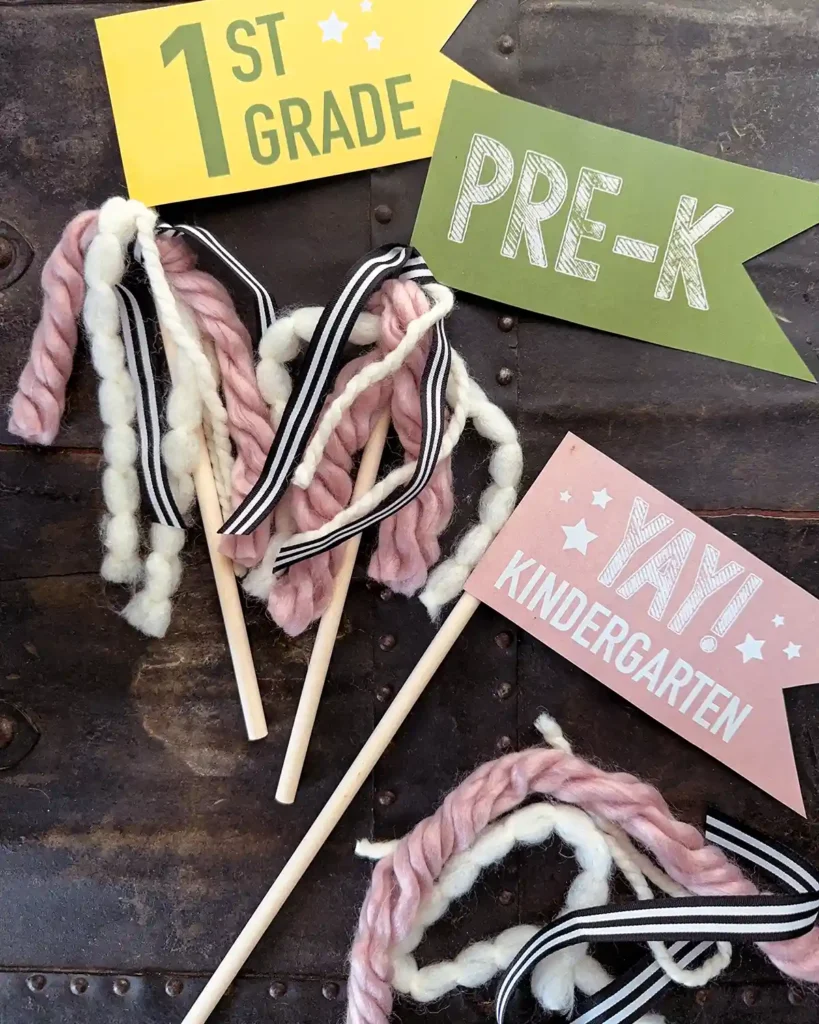 Adding yarn and ribbon to embellish the back to school banners (paper flags for first grade, pre-k, and kindergarten attached to dowels)