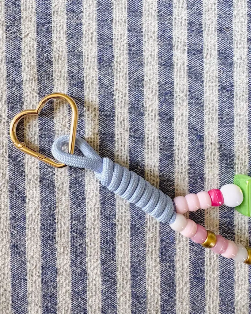 Attaching a gold, heart carabiner to the end of the beaded paracord to make our bag charms