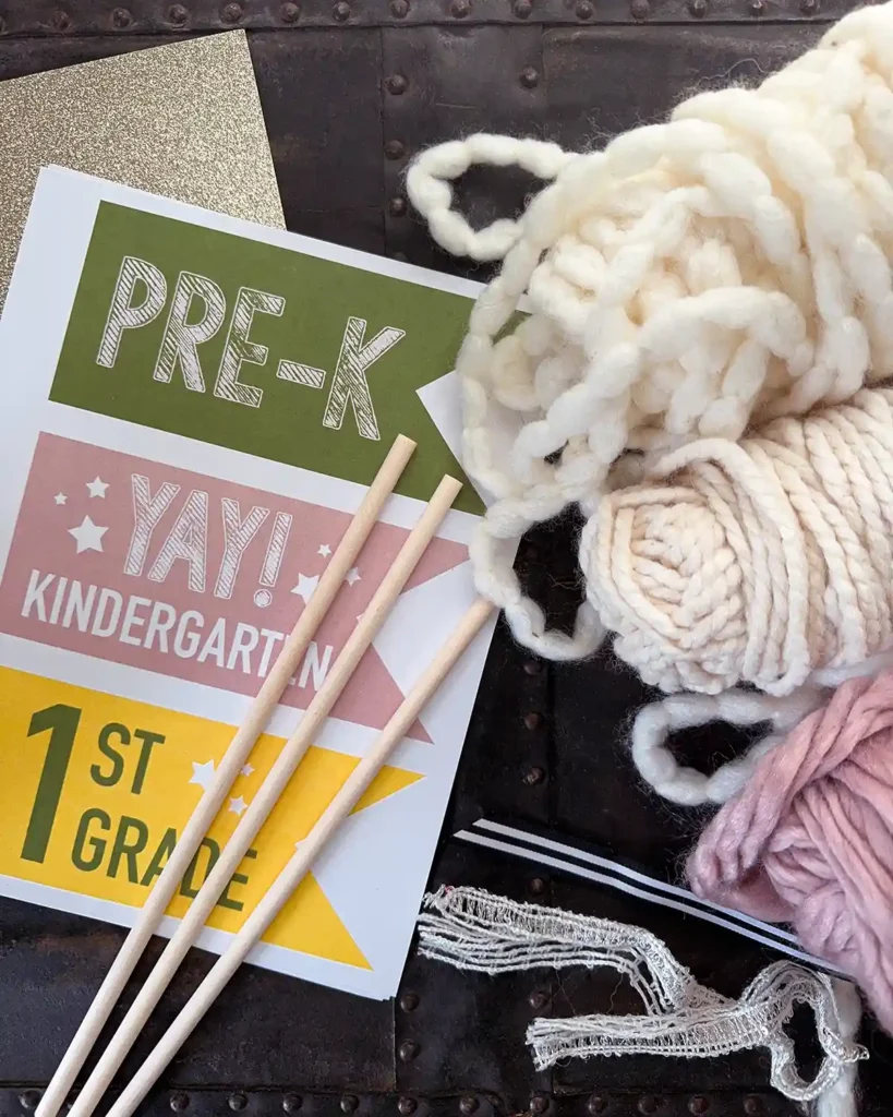 Supplies for making back to school pennant flags including printed flags, glittery paper, wooden dowels, and a collection of yarns and ribbons