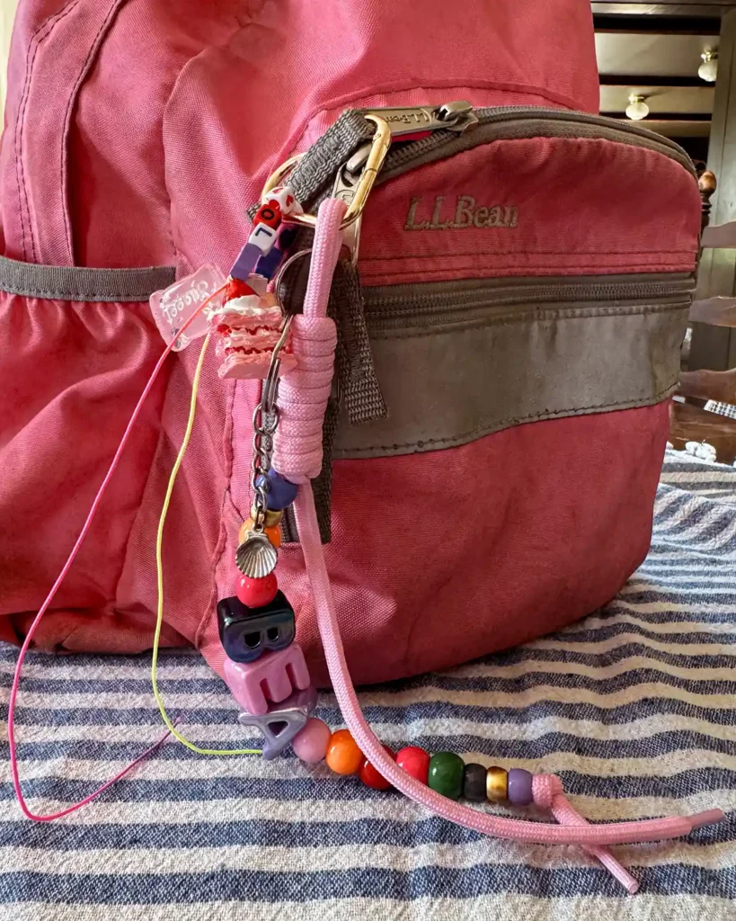A pink LL Bean backpack with a large, bubble letter name keychain attached to it
