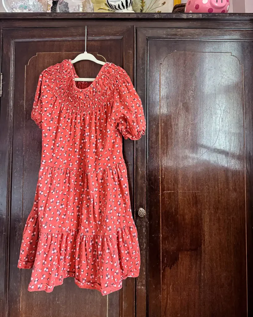 A red kid's dress hanging on the outside of a dark stained, wood wardrobe just before starting the decluttering process
