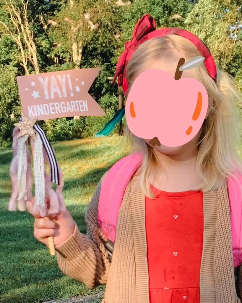 A kindergartener on her first day of school holding a first day of kindergarten flag