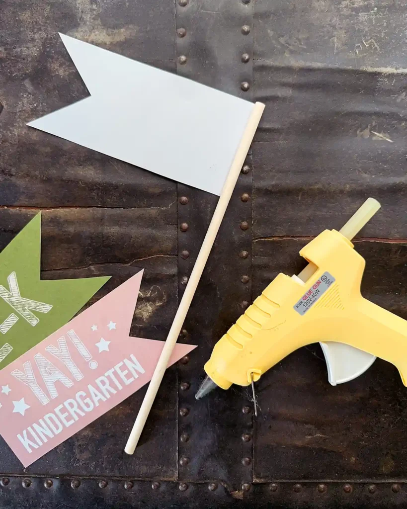 Using a hot glue gun to attach the paper flags to the wooden dowels