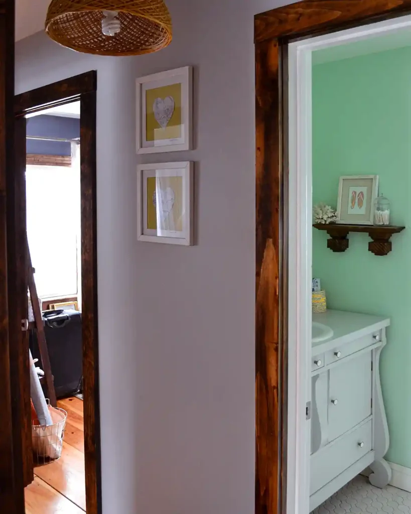 A second floor hallway with doors open to bedrooms and a bathroom, woven light fixture hanging from the ceiling, and framed art on the wall