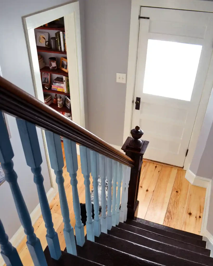 Looking down a renovated staircase with blue balusters towards a white front door and first floor hallway with pine floors