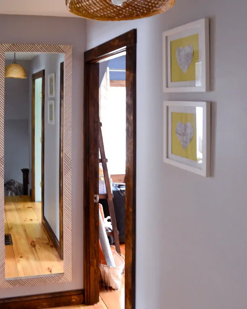 A second floor hallway after remodeling, featuring a DIY framed mirror at the end of the hall, open bedroom doors, wide pine flooring, greige painted walls and dark stained trim