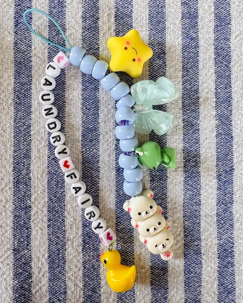 Stringing letter beads (says "laundry fairy"), pony beads, and charms along some string to make bag flair