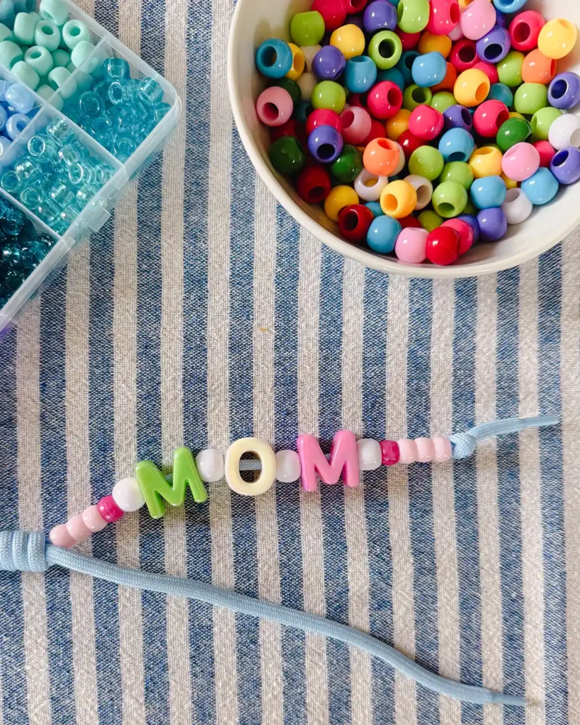 Stringing large letter beads onto paracord to spell "Mom", also used pink and white pony beads to fill along the paracrod keychain