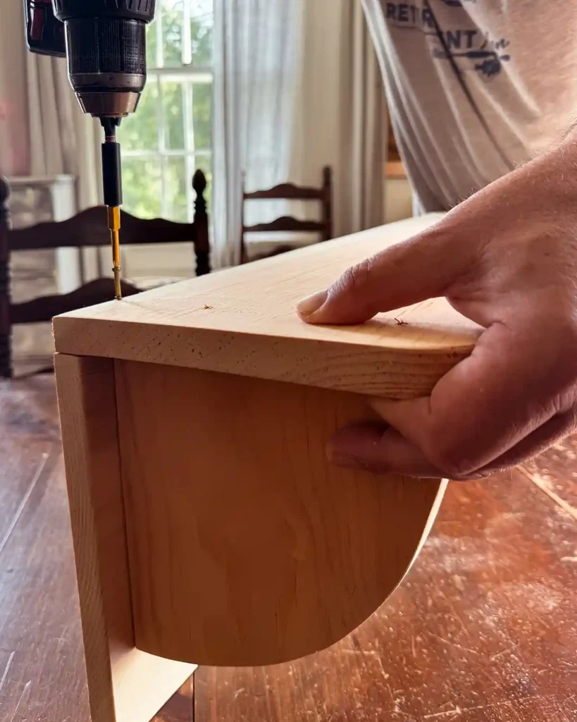 Attaching the top shelf to the shelf brackets of the wall-mounted hanging clothes rack using a cordless drill and screws