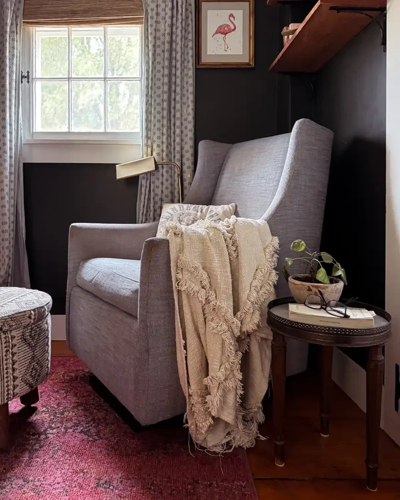 A cream colored textured throw blanket draped over the arm of a light blue glider with side table and upholstered footstool nearby
