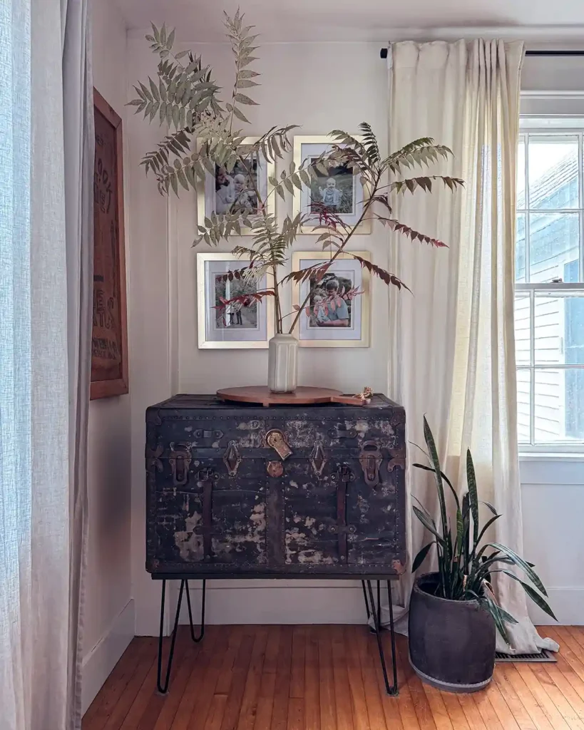 Fall decor in a dining room with a vase of sumac branches sitting on a black trunk in the corner