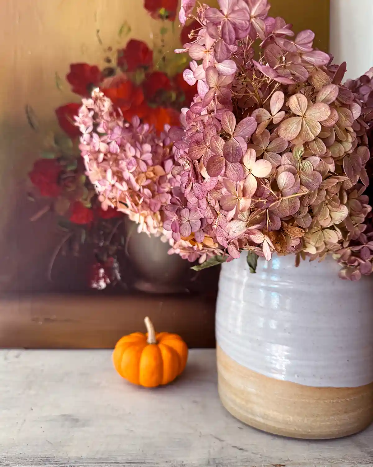 Decorating for fall with a Farmhouse Pottery vase filled with light pink hydrangeas and a small pumpkin sitting beside the vase