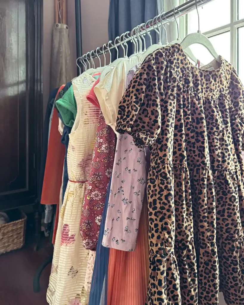 A dress rack in a girls' bedroom filled with dressers of various colors and patterns