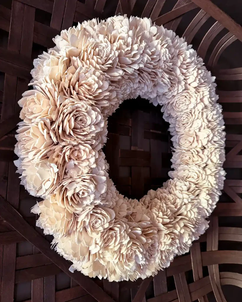 A white, faux floral wreath hanging on a wall layered over top of a tobacco basket