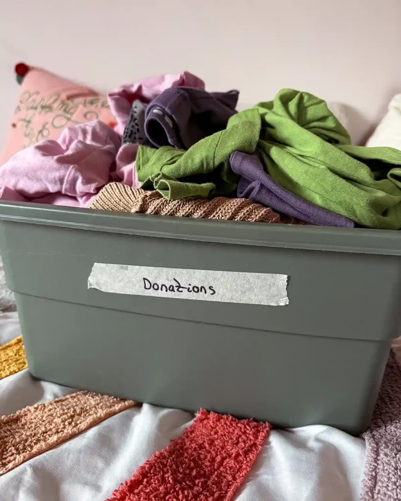 A green tote labeled "donations" filled with various kids clothes that no longer fit