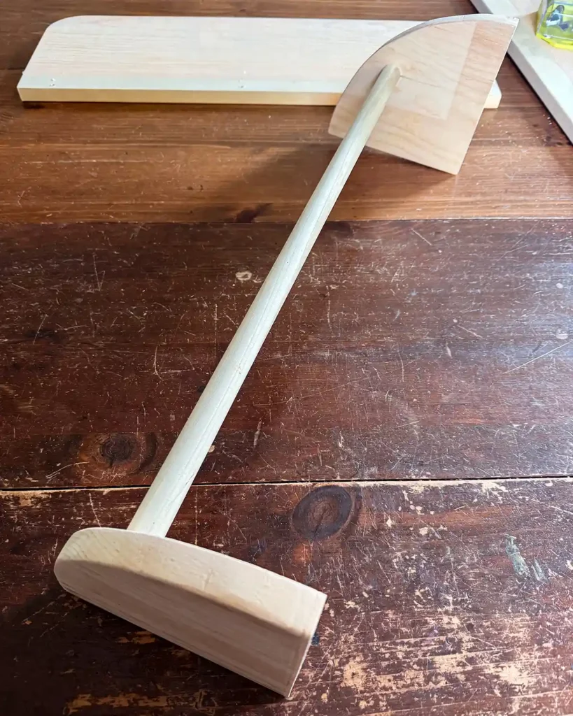 A wooden dowel attached to two wooden shelf brackets, one at each end of the dowel, in the process of making a wall-mounted clothing rack